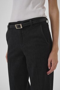Pantalones de mezclilla negros con bolsillos, combinados con un cinturón de cuero negro que tiene una hebilla plateada. Diseño clásico con un corte recto.