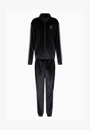 Tuta in velluto nero con colletto alto e frontale con zip. I pantaloni presentano polsini elasticizzati e strisce laterali. Piccolo logo nella zona del petto della giacca.