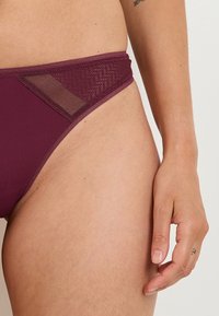 Bas de bikini bordeaux avec un accent en maille texturée, design taille basse, tissu lisse et coutures plates pour un look sans coutures.