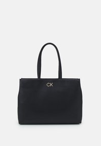Czarna skórzana torba typu tote z dwoma długimi uchwytami, ozdobiona złotym logo „CK” na przodzie. Gładka tekstura i usztywniony kształt.