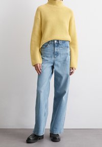 Żółty prążkowany sweter z golfem w połączeniu z jasnoniebieskimi spodniami o wysokim stanie i prostych nogawkach. Czarne, masywne mokasyny dopełniają stylizację.