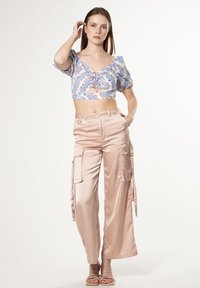 Lichtblauw cropped blouse met pofmouwen en paisleypatroon, gecombineerd met lichtroze satijnen cargo-broek met zakken en zijstrikjes.