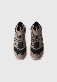 Buty do biegania po szlakach w kolorze brązowym i czarnym, z teksturowaną cholewką, minimalistycznym designem, systemem bezsznurowym oraz solidną podeszwą zapewniającą przyczepność.