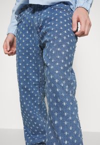 Denimfarkut, joissa on kulutettu pinta, vaaleansininen väri valkoisilla pistekuvioilla ja hapsujen reunoilla saumoissa.