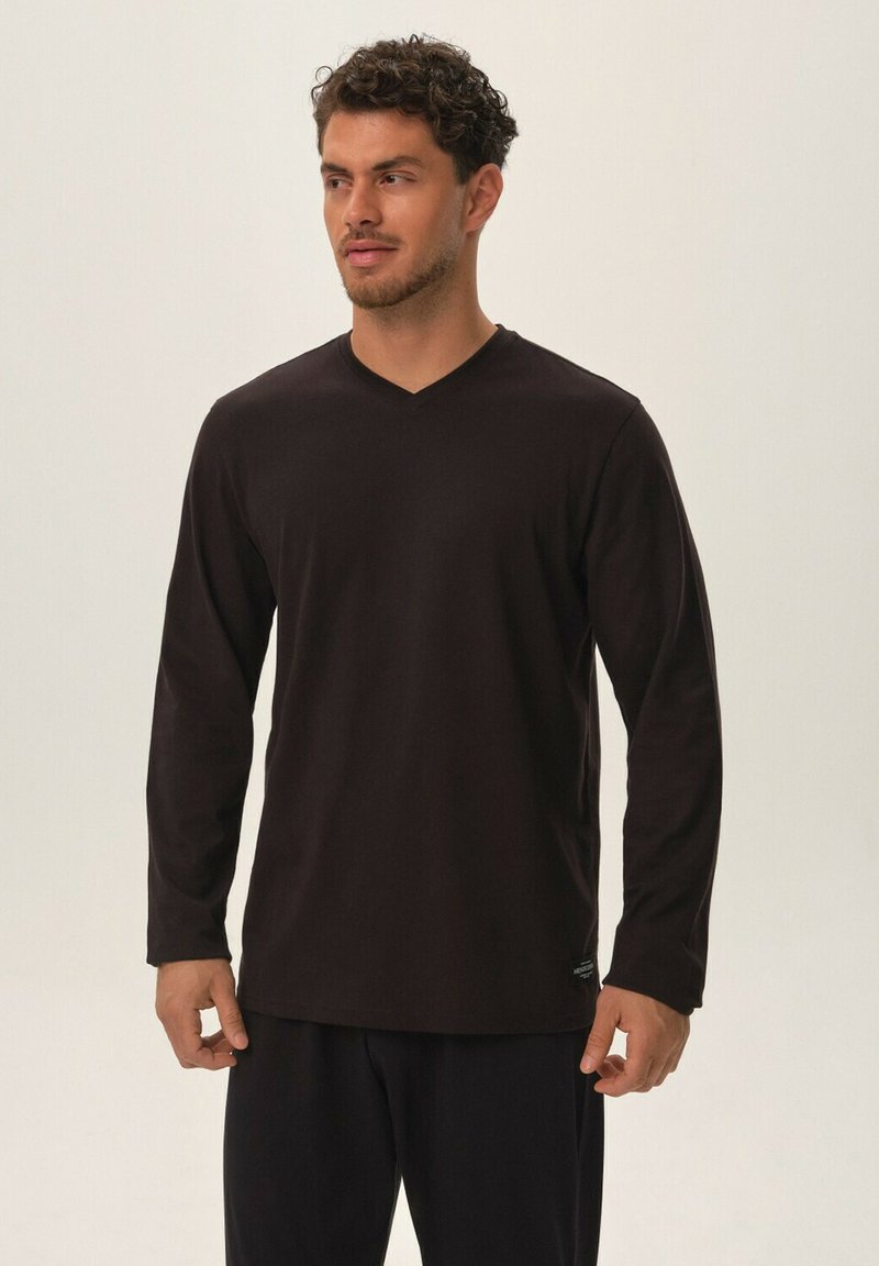 Czarna bluzka z długim rękawem i dekoltem w serek, wykonana z miękkiego materiału, charakteryzująca się luźnym fasonem i subtelną metką marki przy dolnej krawędzi. Brak wzorów lub akcentów.