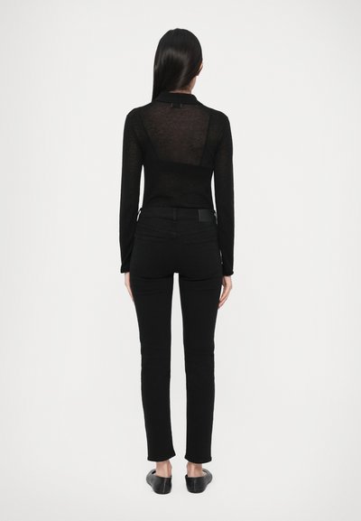 Μαύρο, διαφανές τοπ με μακριά μανίκια και γιακά, σε συνδυασμό με εφαρμοστά μαύρα τζιν. Η εμφάνιση είναι απλή, με ομαλή υφή και χωρίς ορατά σχέδια.