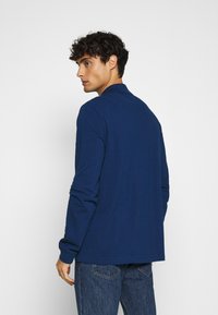 Marineblaues Langarmhemd mit Kragen, gerade geschnitten und aus strukturiertem Stoff. Kombiniert mit hellblauen Jeans.
