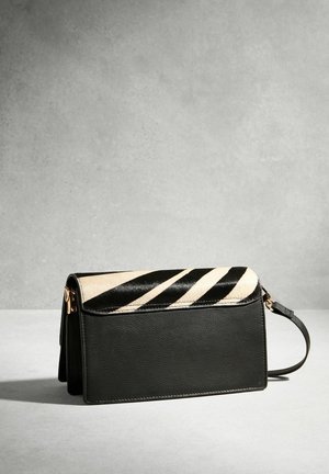 Čierna kožená kabelka do ruky so zipsom s pásikmi zebry a zápästným remienkom, zobrazená na svetlosivom povrchu na sivom pozadí.