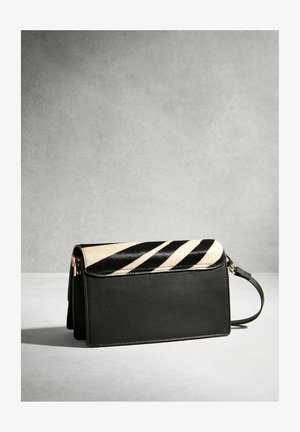 Geantă clutch din piele neagră cu clapetă în dungi de zebră și curea pentru încheietură, expusă pe o suprafață gri deschis, pe fundal gri.