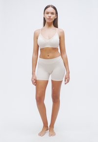 Μπεζ μπραλέτ με δαντελωτό τελείωμα και ταιριαστό σορτς ψηλής μέσης, κατασκευασμένα από λείο, ελαστικό ύφασμα. Χωρίς ορατά κούμπωμα.