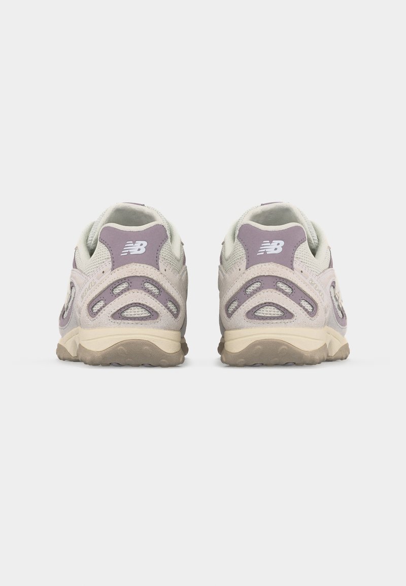 Par de zapatillas New Balance beige y moradas mostradas desde atrás sobre un fondo gris liso.
