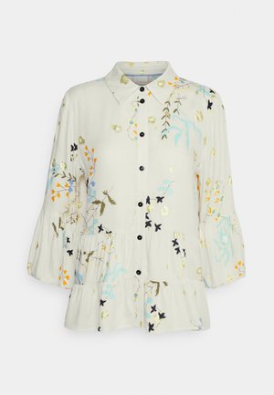 Hellblaue, blumenmusterierte Bluse mit durchgehender Knopfleiste, Kragen und puffigen Ärmeln; sie hat einen Rüschensaum und schwarze Knöpfe.