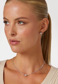 Ensemble de bijoux en argent comprenant un délicat collier en chaîne avec un pendentif rond texturé et des boucles d'oreilles à clous assorties avec des accents scintillants.