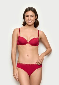 Red lace-trimmed bra with matching brief. The bra features a scalloped design, underwire support, and adjustable straps. Soft texture.