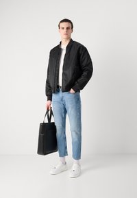 Fekete bomber dzseki, fehér ing, világoskék, kunyhósodott farmernadrág és fehér sportcipő. Fekete táska, fogantyúkkal. Egyszerű, modern dizájn.