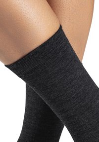 Schwarze Socken mit ribbeltem Bund, aus strukturiertem Stoff, die auf übereinander geschlagenen Beinen gezeigt werden und die dunkle Farbe sowie das Material zur Geltung bringen.