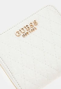 Portafoglio bianco trapuntato con motivo in rilievo, caratterizzato da un logo dorato con la scritta "GUESS EST 1981" sulla parte anteriore. Chiusura con zip e minuteria dorata.