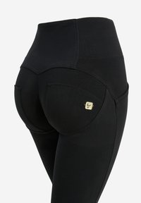 Leggings negros de talle alto con una textura suave, que presentan costuras decorativas y un pequeño detalle de hardware dorado en un bolsillo trasero.