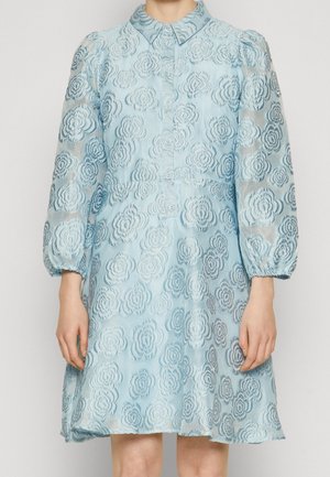 Jasnoniebieska przezroczysta sukienka z kwiatowym koronkowym wzorem, długimi bufkami na rękawach, zapinana z przodu na guziki, z kołnierzykiem, noszona przez stojącą osobę.