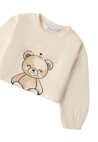 Sudadera corta de color crema con mangas largas y abullonadas. Presenta un gráfico de un oso de dibujos animados y el texto "Sonrisa Dulce" en rosa. Tejido suave y liso.