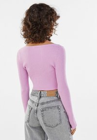 Fitted, ribbed pullover in light pink with long sleeves and wide neckline. Paired with high-waisted, light grey denim jeans.