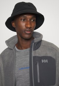 Szary polarowy sweter zapinany na zamek z ciemnoszarymi akcentami, z kieszenią na piersi. Czarne kapelusz typu bucket dopełnia całość. Szary t-shirt w paski pod spodem.