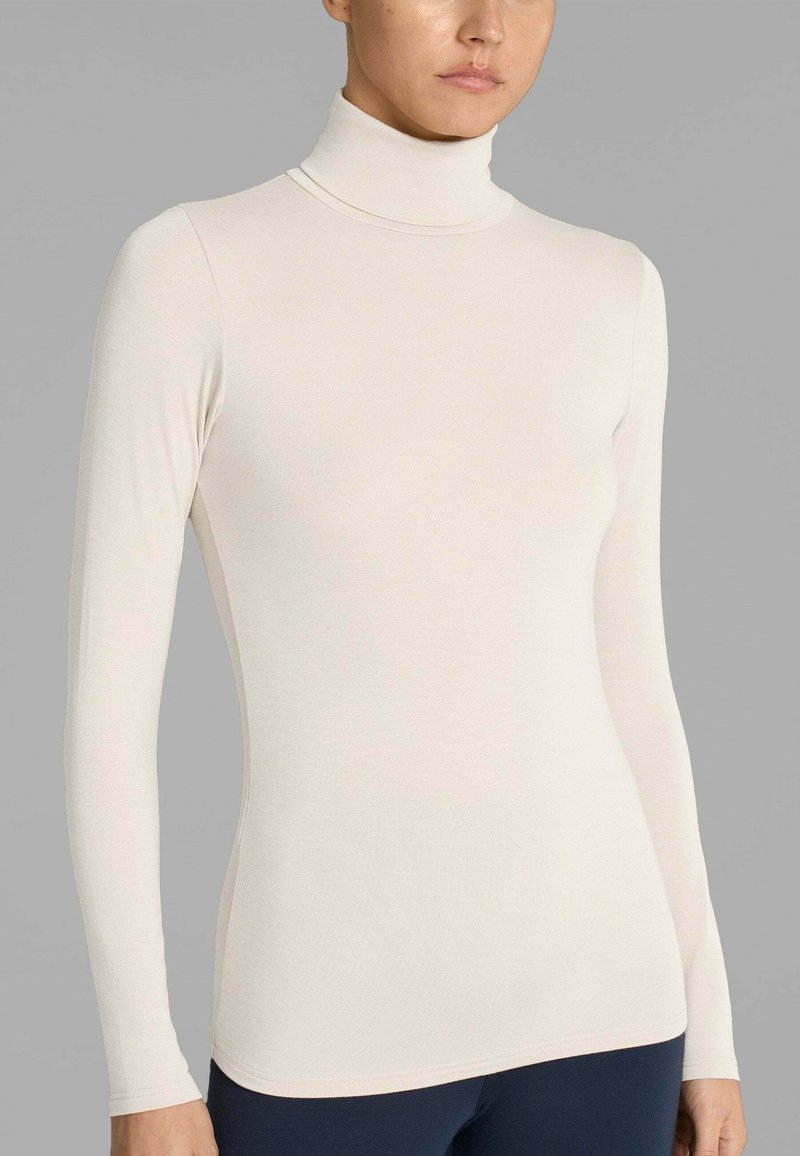 Maglia a maniche lunghe color beige chiaro con collo alto, realizzata in tessuto morbido e liscio, dalla forma aderente e con cuciture minime, caratterizzata da un collo a costine.