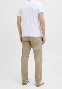 Valkoinen t-paita lyhyillä hihoilla, rento istuvuus, yhdistetty beigenvärisiin housuihin, pehmeästä materiaalista, täydentää vaaleat kengät, joissa on ruskea pohja.