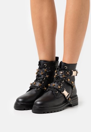 Czarne skórzane botki za kostkę z wieloma ozdobnymi paskami z złotymi ćwiekami, bocznym zamkiem błyskawicznym i grubą podeszwą zapewniającą lepszą przyczepność.