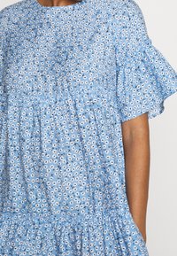 Blå blommönstrad klänning med rund halsringning, korta volangärmar och hopkrupna lager för en avslappnad passform. Tillverkad av bomullsblandning.