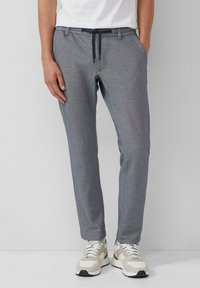 Grijze joggerpants van zachte stof, met een tailleband met trekkoord, zijzakken en een taps toelopende pasvorm, gecombineerd met beige sneakers.