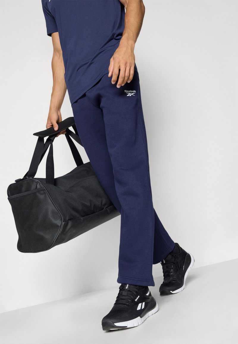 Sudadera azul marino con un diseño ajustado, combinada con una bolsa de lona negra y zapatillas negras con acentos blancos.