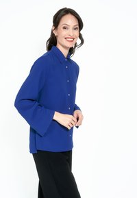 Blå skjorta med knapp-up, krage och utsvängda ärmar, gjord av ett slätt tyg, matchad med svarta byxor. Enkelt design, utan mönster.