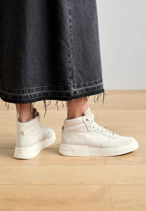 Hochfinanz-Sneaker aus weißem Leder mit strukturierten Einsätzen, kontrastierender Sohle und weicher Knöchelpolsterung, getragen mit einem fransigen schwarzen Jeansrock.