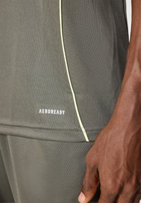 Tejido atlético gris oscuro con una textura lisa, que presenta una franja de acento verde claro y la palabra "AEROREADY" en blanco.