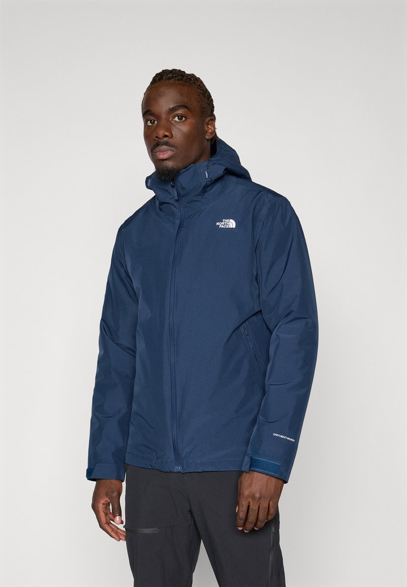 Jachetă impermeabilă de marină cu fermoar frontal și glugă. Caracteristici: logo-ul The North Face pe piept și manșete elastice pentru o potrivire strânsă.