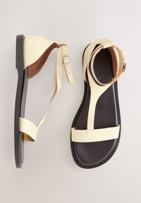 Beeži nahast sandaalid, kus on segu mati ja läikiva tekstuuriga, pandlaga kinnitusega ning pruunist kummist tallaga, mis on minimalistliku disainiga.