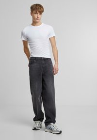 Hvit T-skjorte med rund hals, kombinert med høyt liv, løstsittende, mørkegrå jeans. Modellen har på seg sølvfargede joggesko med blå detaljer.