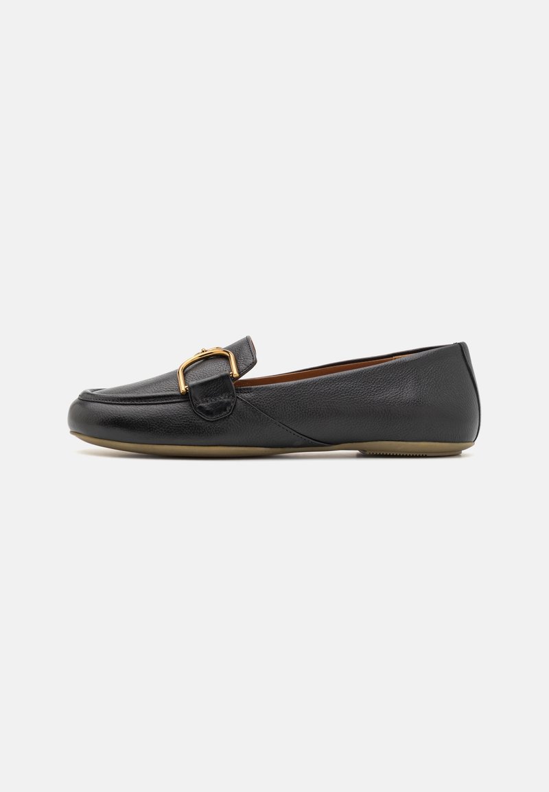 Mocassin plat en cuir noir avec bout arrondi, détail boucle dorée sur le dessus et semelle beige sur un fond clair uni.