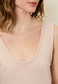 Jasnoróżowy top na ramiączkach z szerokim dekoltem w kształcie łódki i surowymi krawędziami. Miękka, gładka tekstura oraz lekko przezroczysty materiał. Minimalistyczny design.