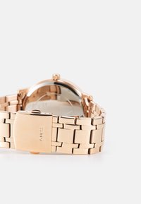 Montre en acier inoxydable doré avec un bracelet à maillons, un boîtier rond et une finition métal poli. Elle dispose d'un fermoir élégant avec une marque.
