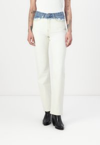 Jeans de cintura alta com um cós de denim azul desbotado e pernas de um bege claro, apresentando um corte reto e detalhes de costura mínimos.