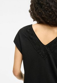 Top nero con scollatura a V, arricchito da una complessa ricamatura circolare testurizzata lungo il colletto, maniche corte e una vestibilità rilassata.