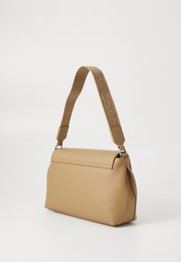 Sac à main beige avec une texture lisse, de forme rectangulaire et une sangle gravée au logo. Présente des détails en acier inoxydable et une fermeture à rabat.