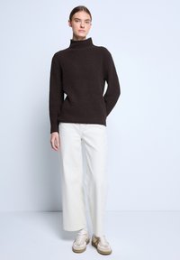 Bruin gebreid pullover met hoge kraag, gecombineerd met roomkleurige wijde broek en beige sneakers, voor een lichte achtergrond.