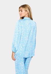 Világoskék pizsama szett virágmintával, hosszú ujjakkal és laza fazonnal. Az anyag sima, enyhe fényű.