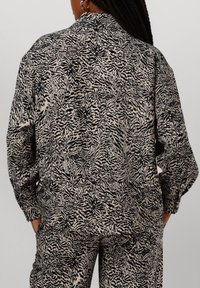 Zwart en crèmekleurig shirt met een ontspannen pasvorm, voorzien van een abstract bladontwerp en lange mouwen. De stof heeft een zachte textuur.
