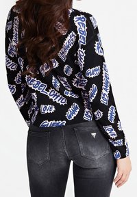 Pull noir avec un texte graphique blanc et bleu, associé à un jean gris foncé avec des poches arrière et des accents de logo. Texture tricotée visible.