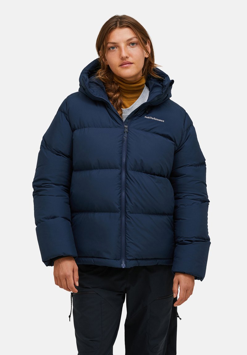 Marineblauer Puffer-Jacken mit Reißverschluss, großer Kapuze und gestepptem Design. Fällt auf durch ein Logo auf der linken Brust und gerippte Bündchen.