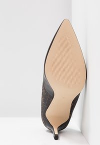 Chaussure à talon haut à bout pointu, semelle beige, petit talon noir et empeigne à motif sombre, taille 37, inclinée contre un coin blanc.